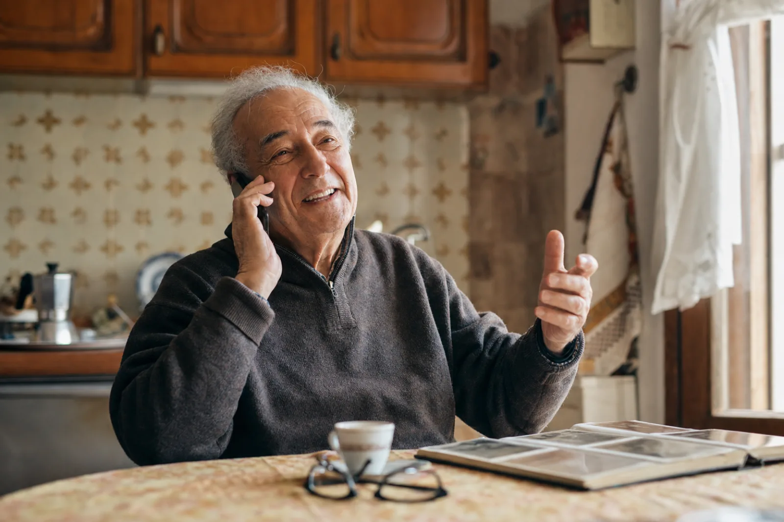 Un signore anziano racconta la sua storia al telefono, seduto al tavolo di casa